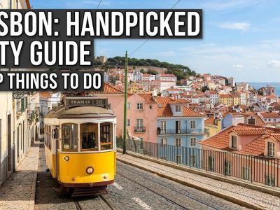 A scenic view looking down a steep, cobbled street in Lisbon featuring traditional colorful buildings and a historic yellow tram.